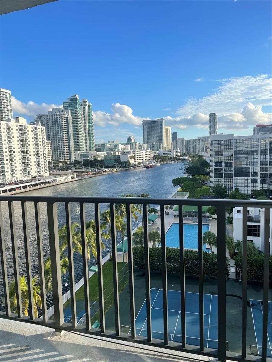 Balcony with dark metal railing, overlooking a waterway, tennis court, and swimming pool