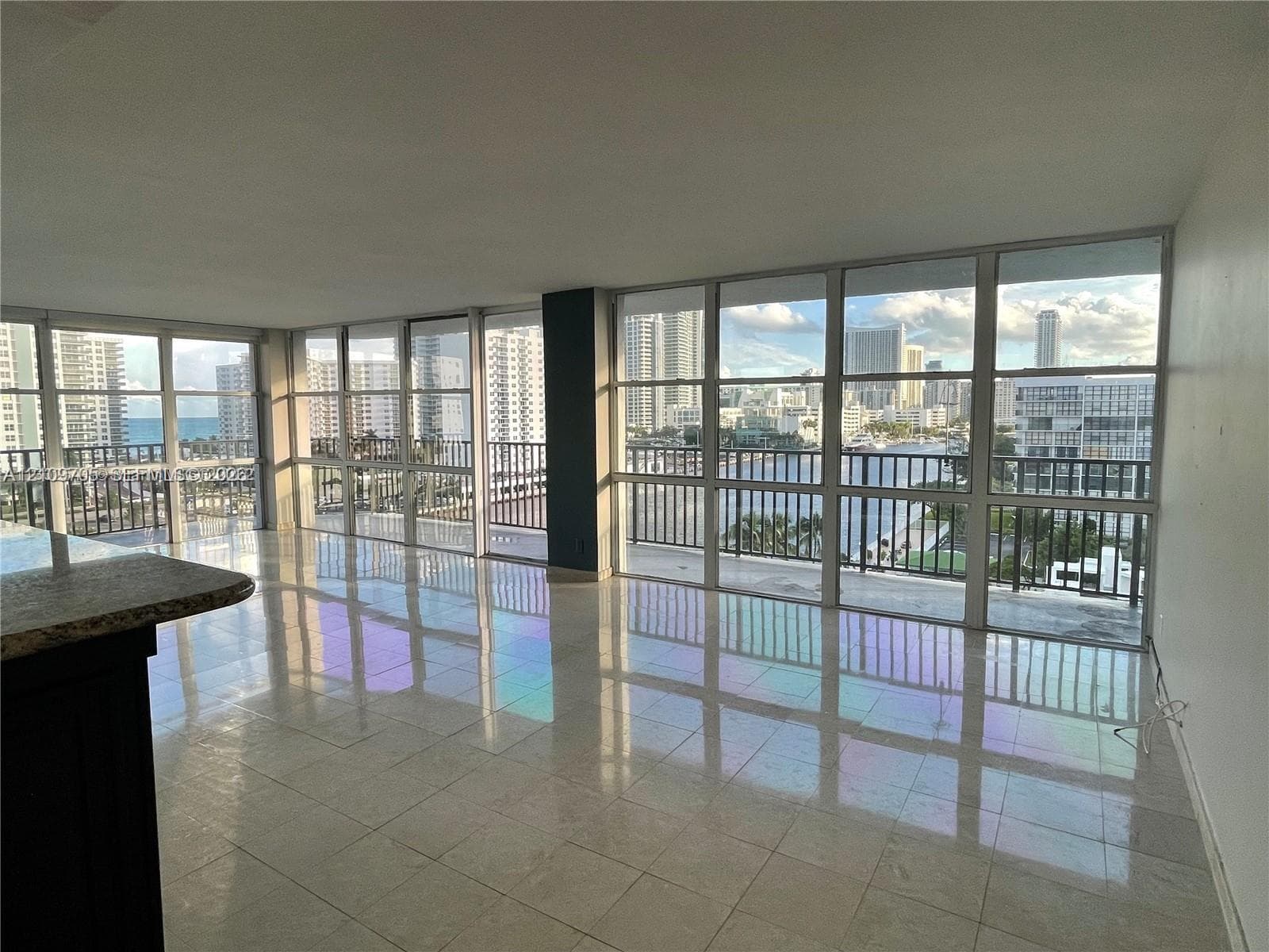 Floor-to-ceiling windows with expansive city and water exposure, polished stone tile flooring, and a private balcony with metal railing