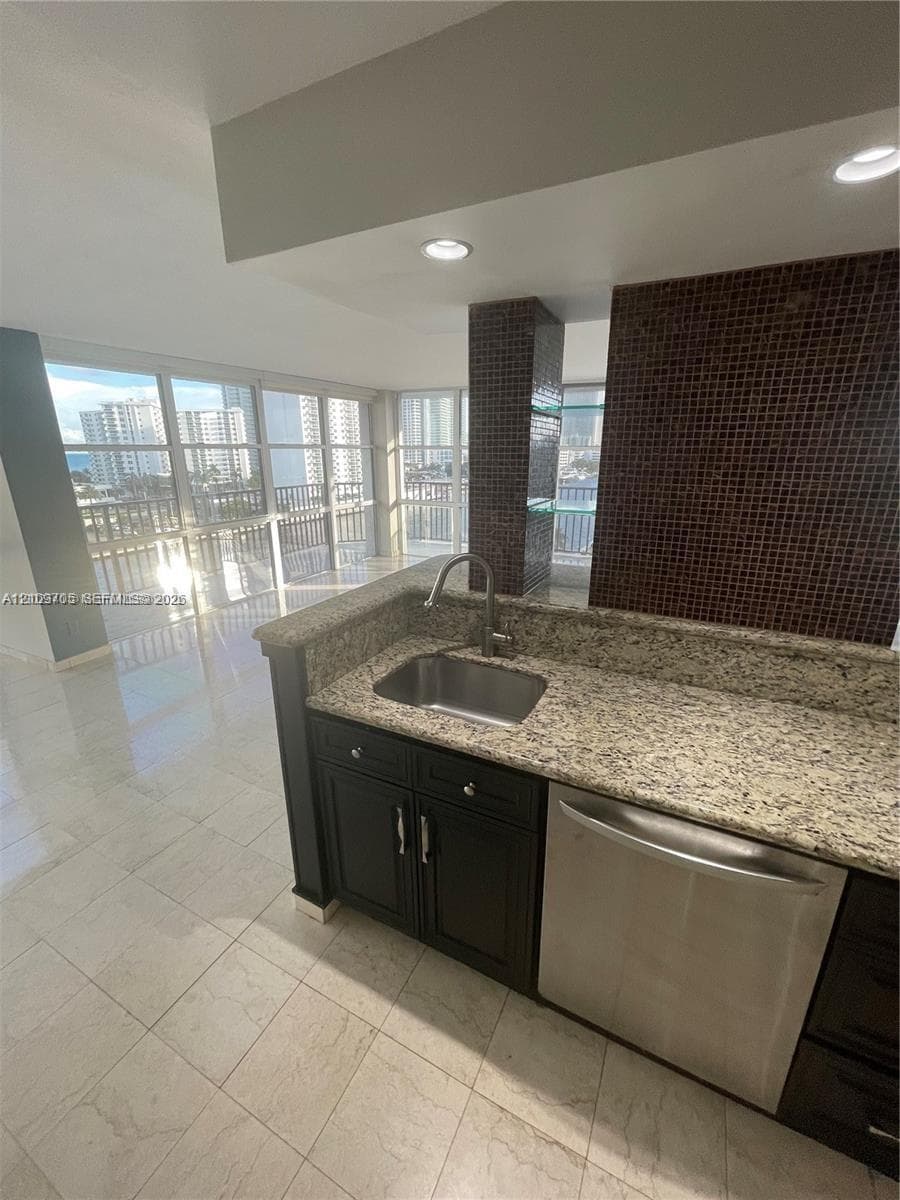 Kitchen featuring stone-finish countertops, stainless steel undermount sink, dark cabinetry, recessed lighting, and mosaic tile backsplash
