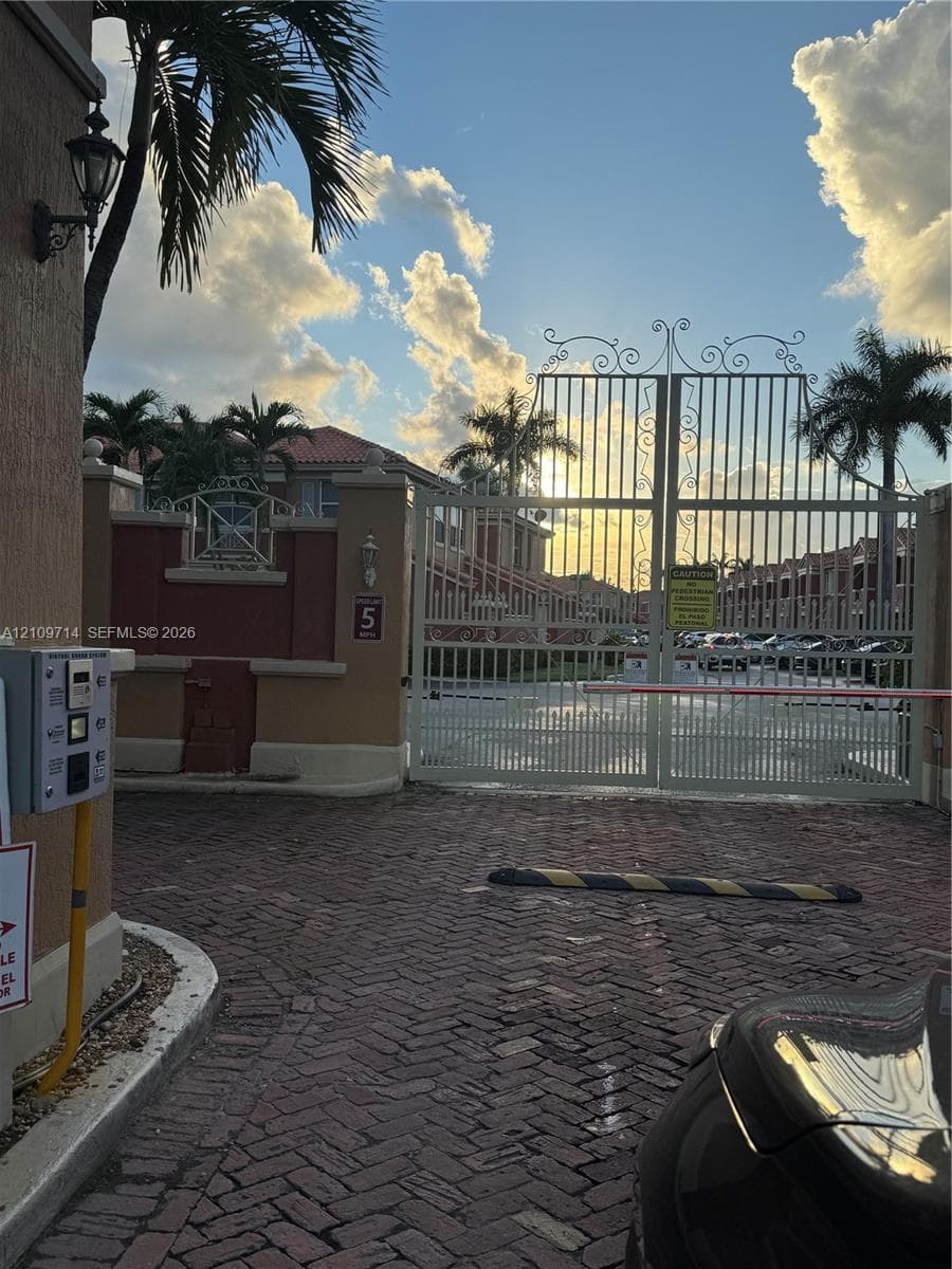 Gated entry featuring iron security gates, electronic access system, brick-paver drive, and decorative stucco pillars