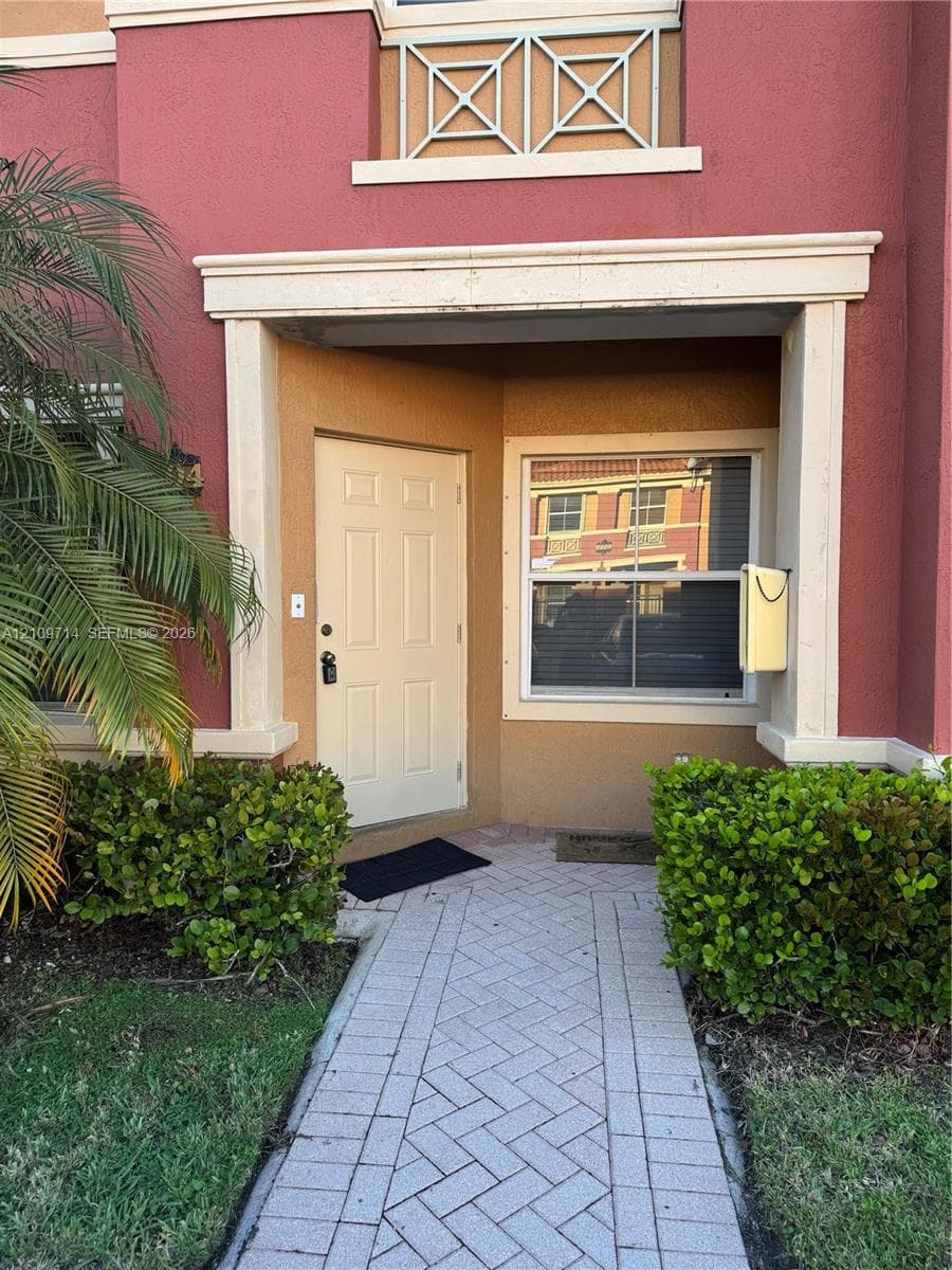 Stucco exterior entrance featuring a paver walkway, decorative railings, and molded trim accents