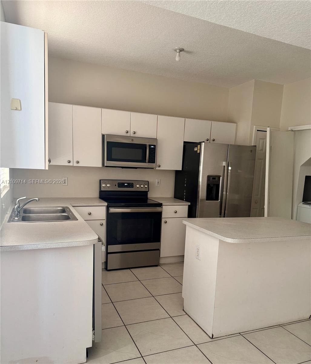 Kitchen featuring white cabinetry, stainless steel appliances, solid-surface countertops, a center island, and ceramic tile flooring