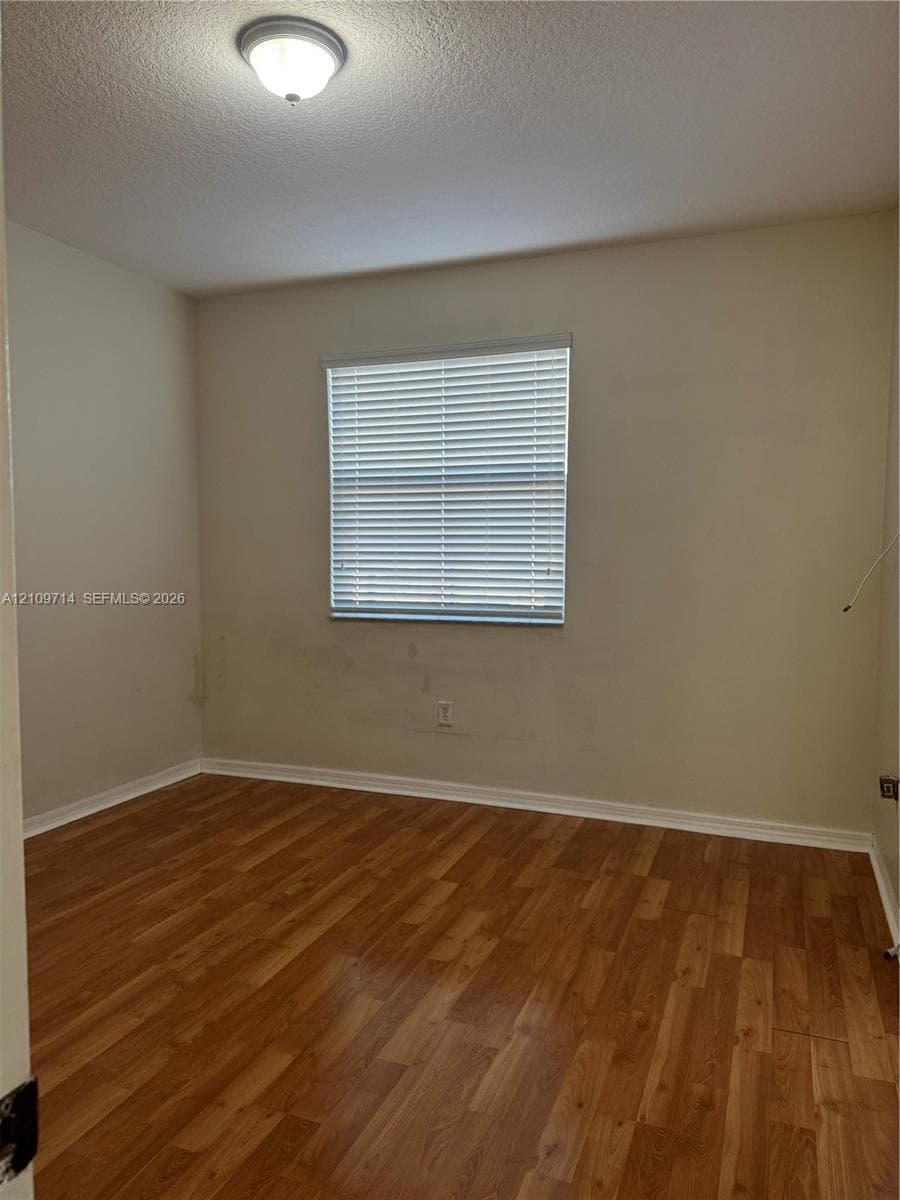 Room featuring wood-finish flooring, a neutral wall palette, an integrated ceiling light fixture, and a window equipped with horizontal blinds
