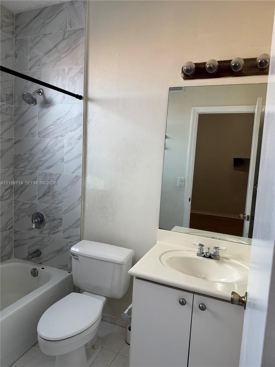 Bathroom featuring a vanity with an integrated sink, wall-mounted mirror, light fixture, and tile shower surround