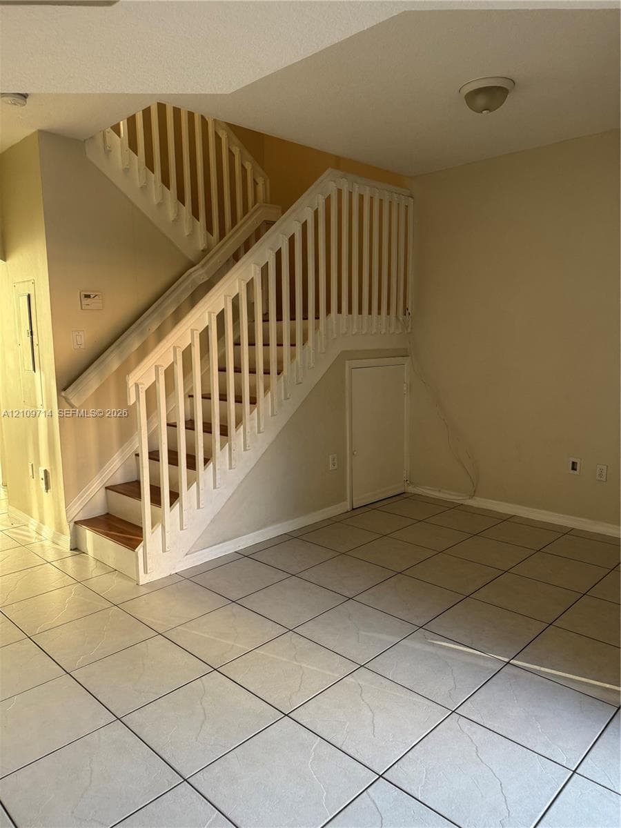 Staircase featuring wood-finish treads and white wooden balusters, neutral tile flooring, and integrated under-stair storage cabinet