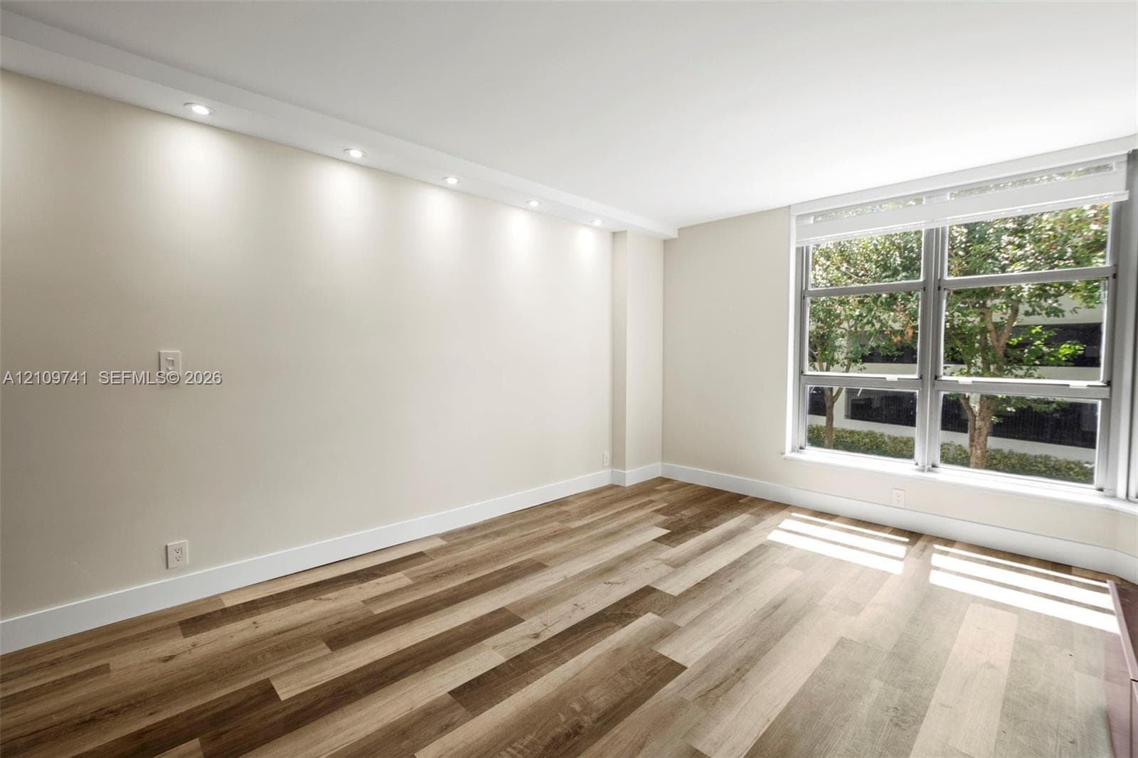 Room featuring wood-finish flooring, recessed ceiling lighting, and large windows with integrated blinds