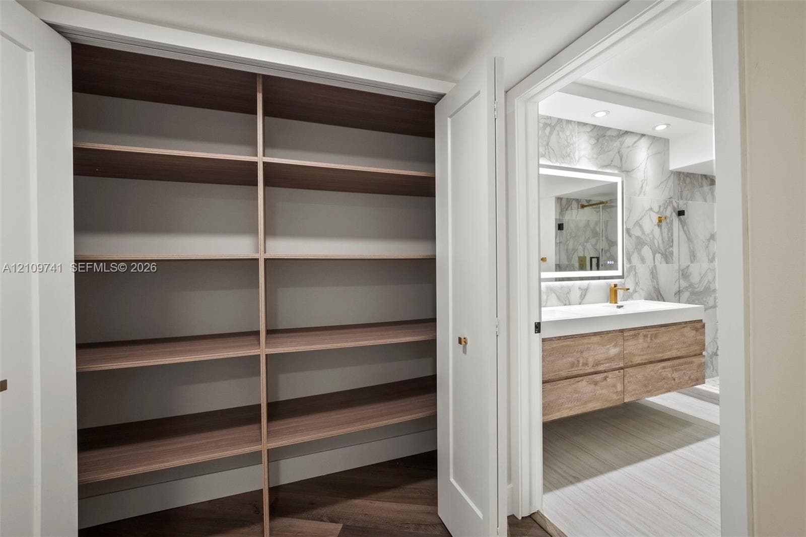 Built-in storage closet featuring wood-finish shelving, and bathroom with a floating wood-finish vanity, integrated rectangular sink, wall-mounted faucet, and stone-finish wall tile