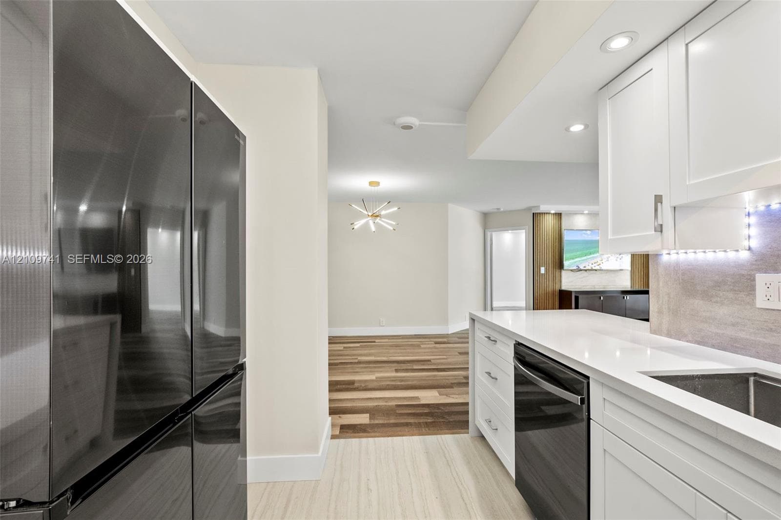 Kitchen featuring white shaker-style cabinetry, quartz countertops, integrated under-cabinet lighting, a stainless steel dishwasher, and a full-size dark-finish refrigerator