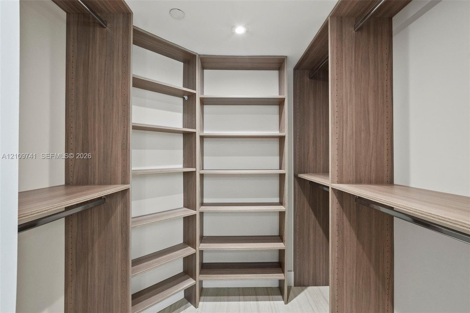 Custom walk-in closet featuring wood-finish cabinetry, built-in shelving units, integrated hanging rods, and recessed lighting
