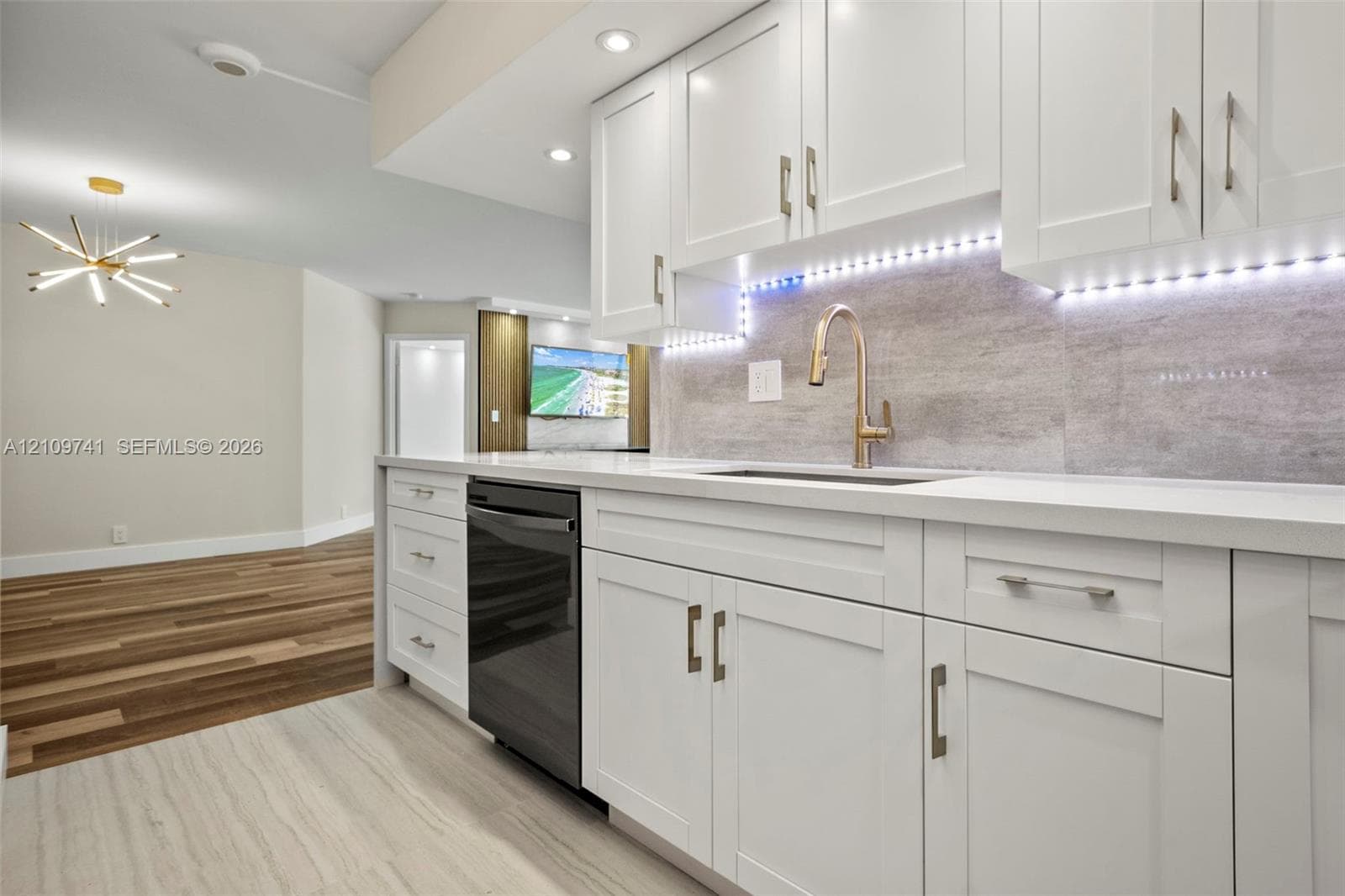 White Shaker-style cabinetry, matte stone-finish backsplash, undermount sink with high-arc faucet, integrated under-cabinet lighting, and wood-finish flooring