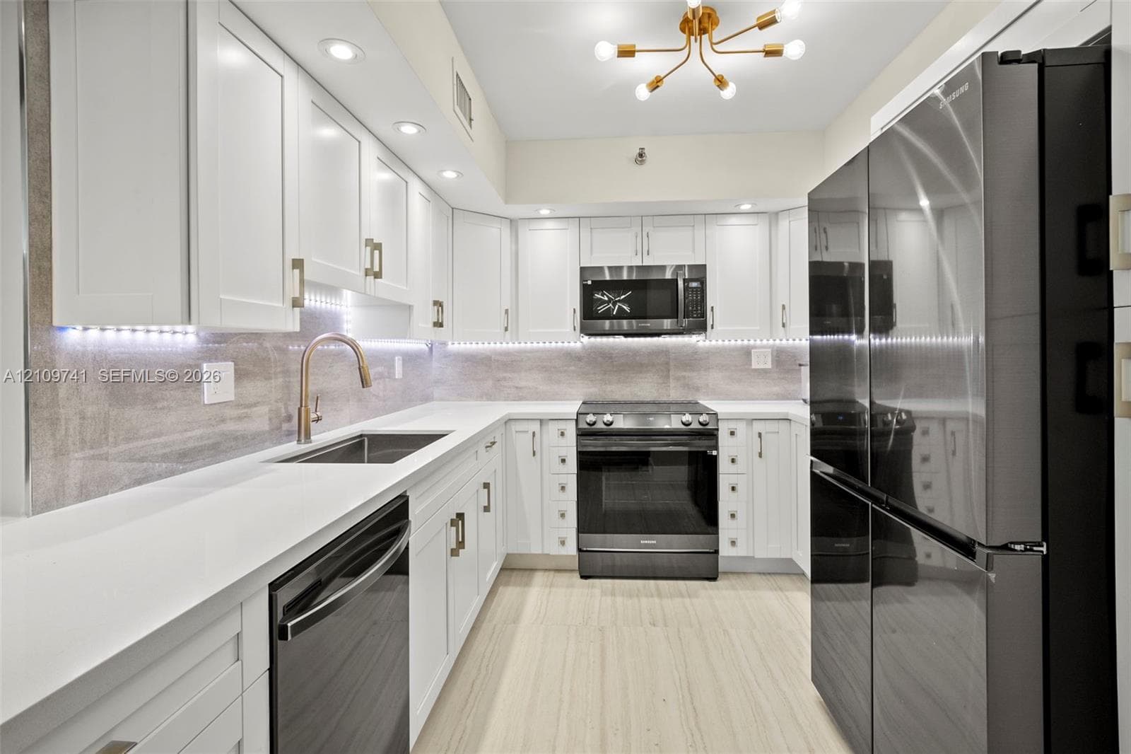 Kitchen featuring white shaker-style cabinetry, stainless steel appliances, stone-surface countertops, under-cabinet lighting, and wood-finish flooring