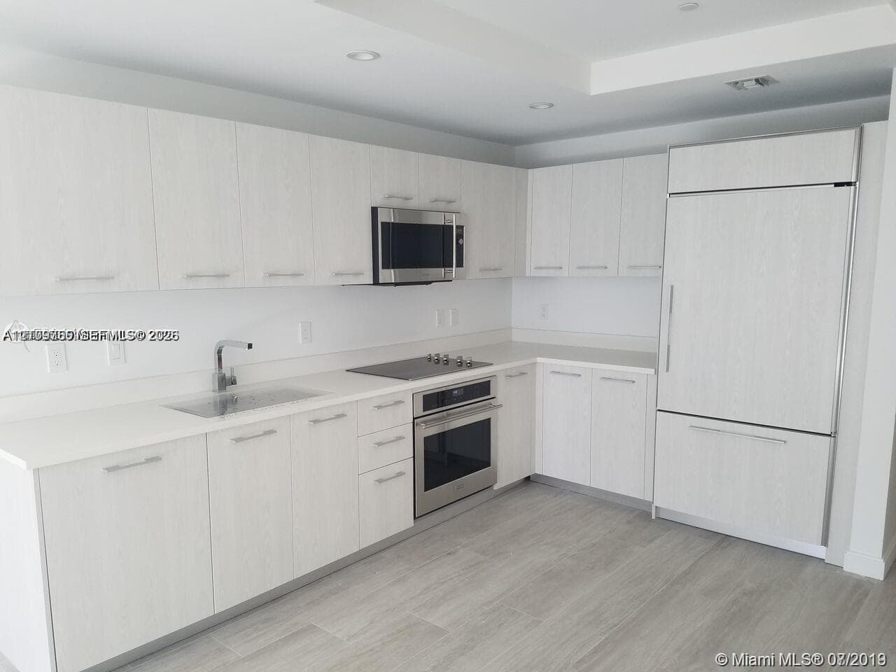 Kitchen featuring light wood-grain cabinetry, solid surface countertops, stainless steel appliances, a flush-mounted cooktop, and wood-finish flooring