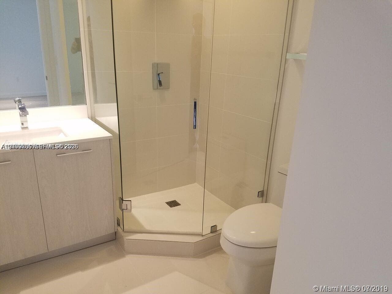 Bathroom featuring a glass-enclosed shower with tile surround, wood-finish cabinetry, countertop sink with metallic faucet, and a wall-mounted shower fixture