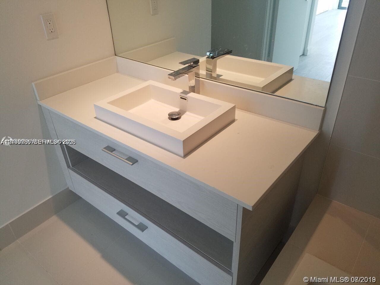 Modern floating vanity with a light wood-finish frame, rectangular vessel sink, solid-surface countertop, and polished chrome faucet