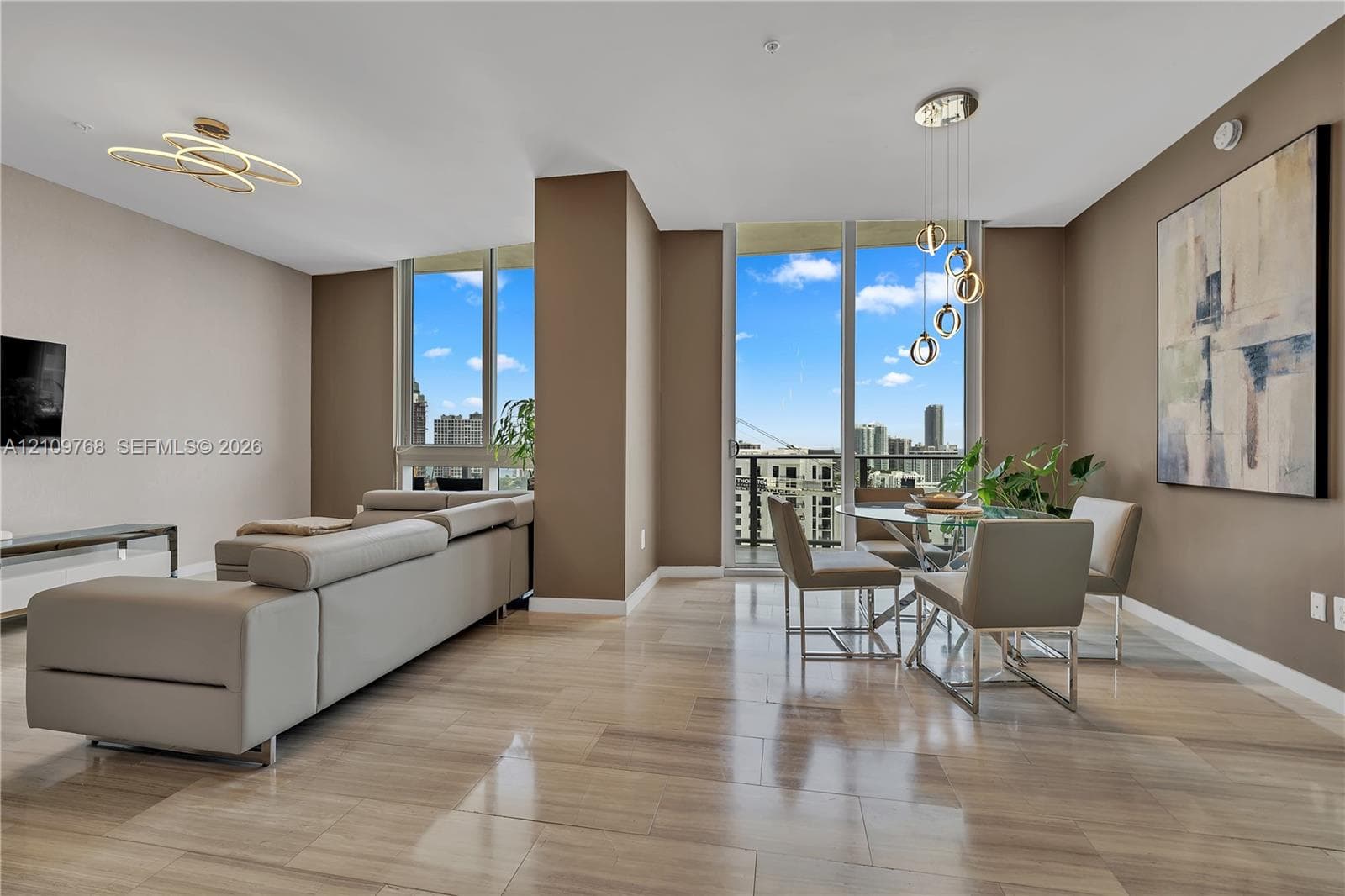 Open-concept interior featuring floor-to-ceiling windows, neutral wall tones, polished stone flooring, modern geometric chandelier lighting, and a private balcony