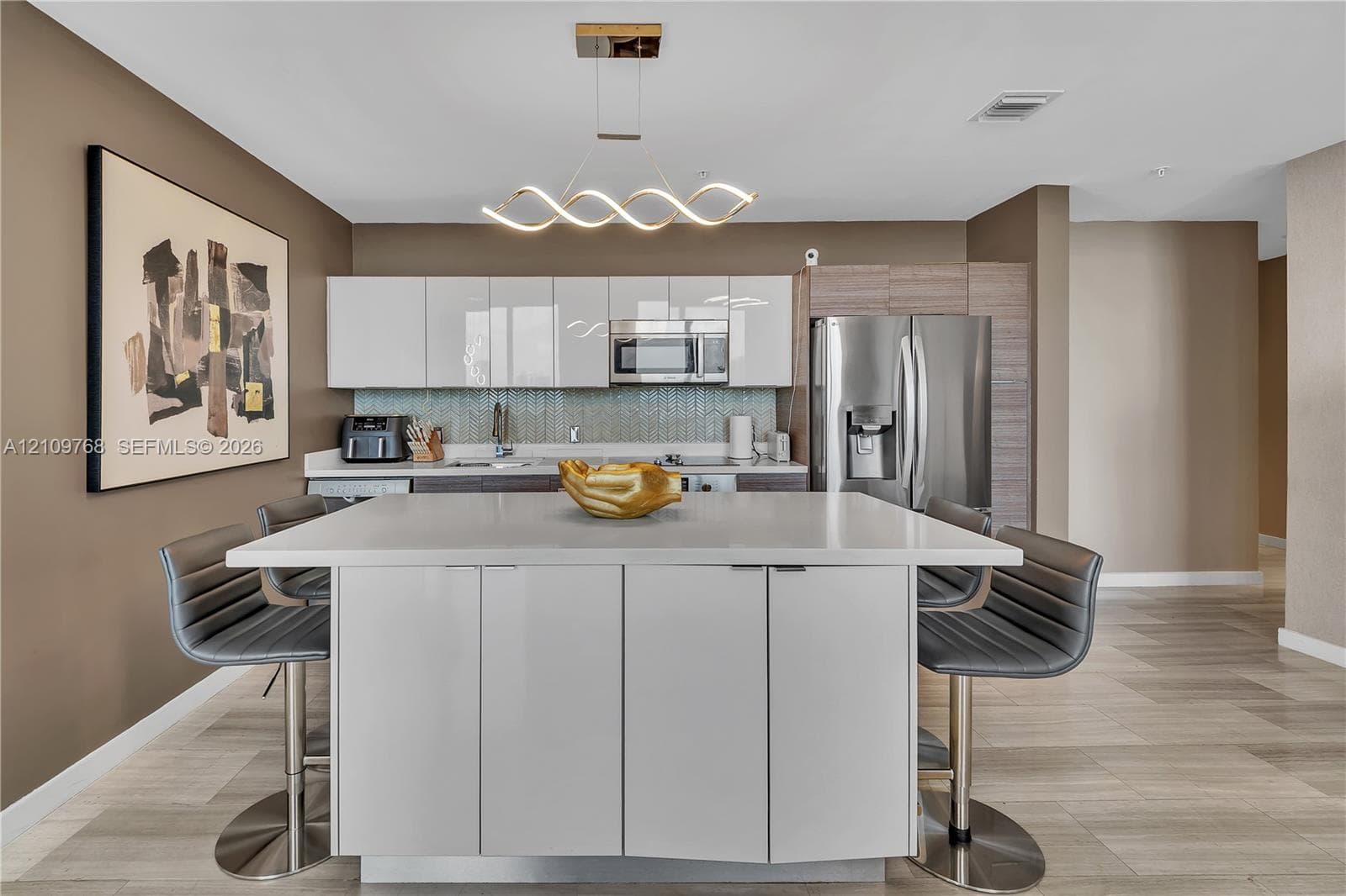 Kitchen featuring a central island with a quartz countertop, high-gloss white cabinetry, stainless steel appliances, a geometric LED pendant light, and tile flooring