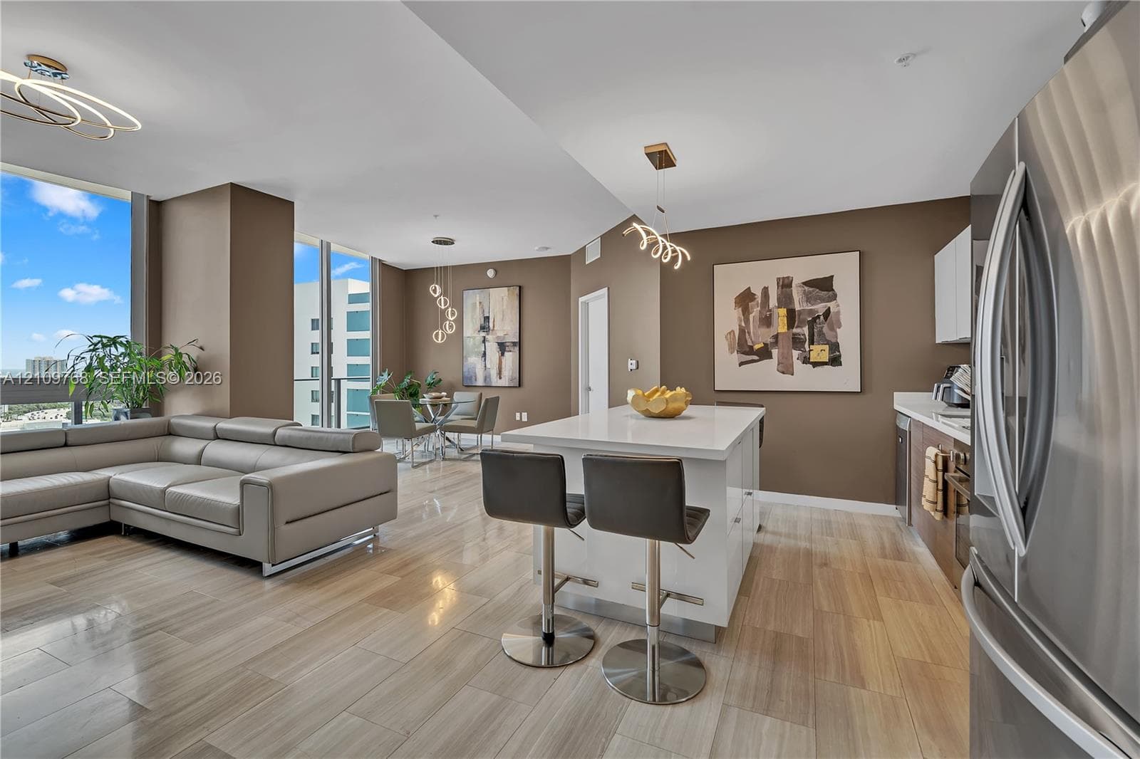 Open floor plan featuring wood-finish flooring, kitchen island with quartz countertop, floor-to-ceiling windows, and modern statement lighting fixtures