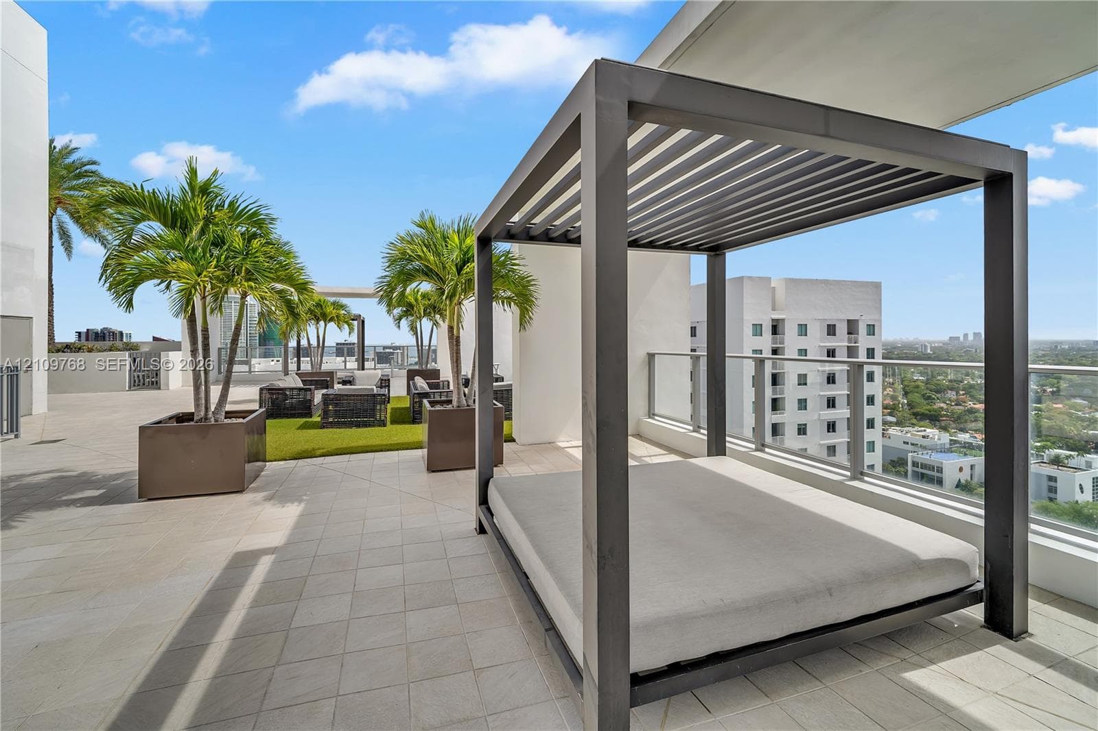 Expansive outdoor terrace featuring light-toned tile flooring, a metal-framed louvered pergola, and a glass panel railing
