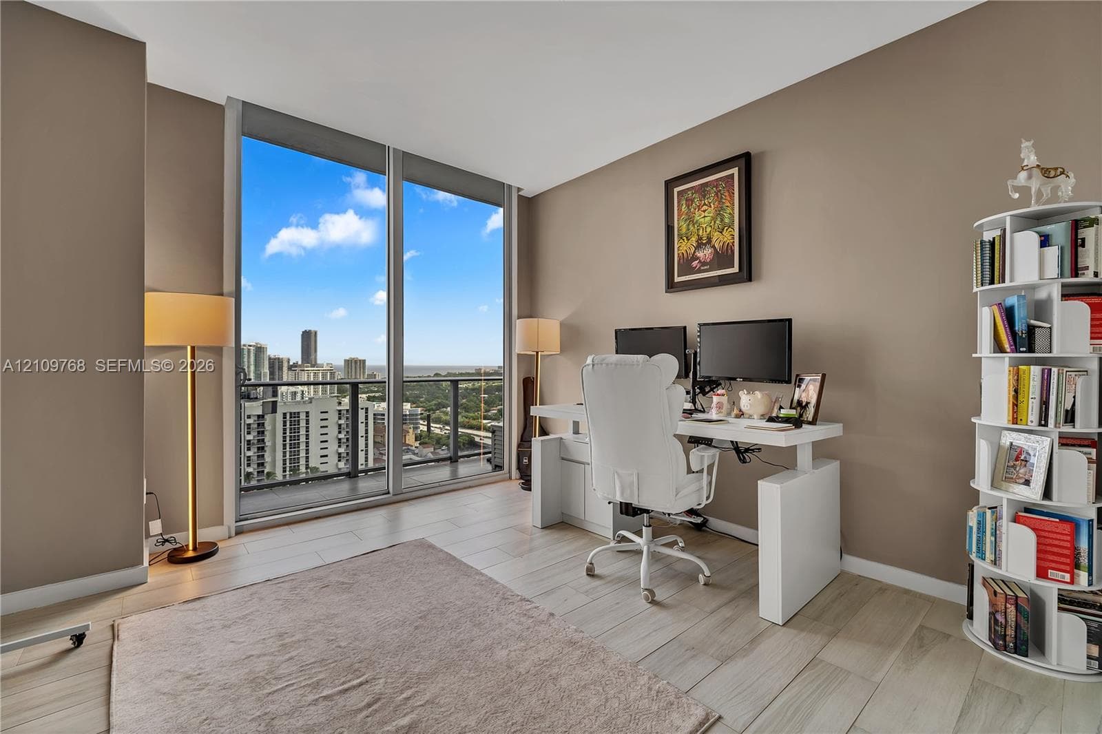 Floor-to-ceiling windows, wood-finish flooring, and glass-paneled balcony access with expansive urban cityscape scenery