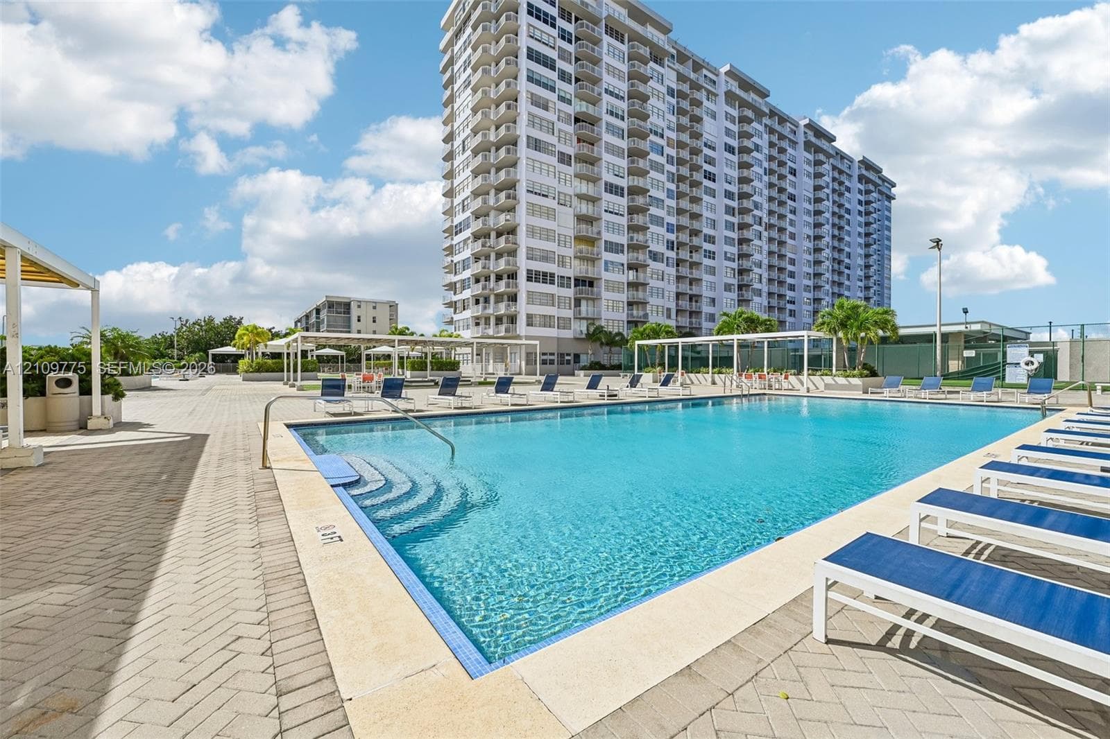 Swimming pool with stone-tiled deck, herringbone-patterned paved patio, and metal-framed shade structures