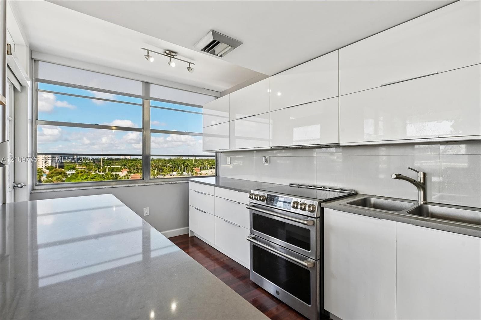 High-gloss white cabinetry, expansive stone countertops, stainless steel dual-oven range, double basin undermount sink, and floor-to-ceiling windows