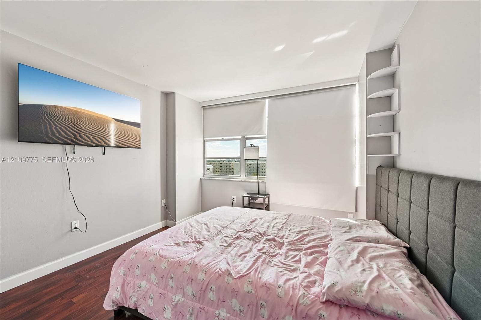 Room featuring wood-finish flooring, multi-pane window with integrated roller shades, and built-in corner shelving