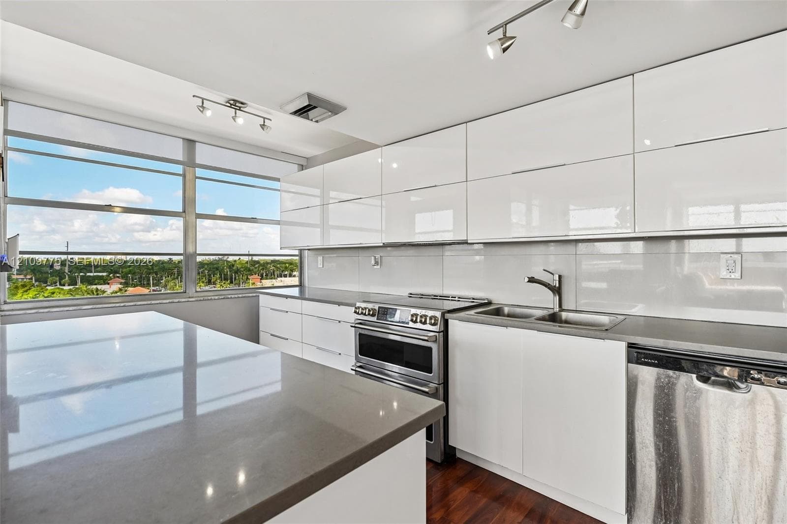Kitchen featuring glossy white flat-panel cabinetry, a stainless steel range, a solid-surface island countertop, and wood-finish flooring, complemented by a large horizontal window