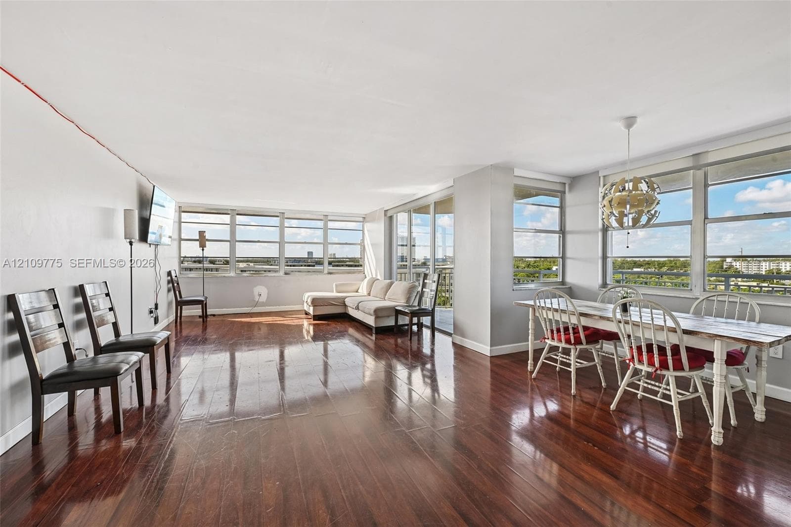 Expansive open-concept living area featuring polished wood-finish flooring, floor-to-ceiling windows, and a built-in overhead light fixture