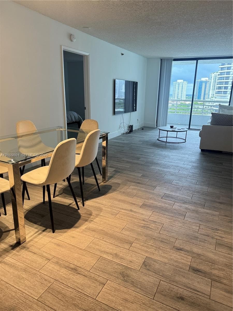 Open-concept interior featuring wood-finish tile flooring, floor-to-ceiling glass sliding doors, and a private balcony