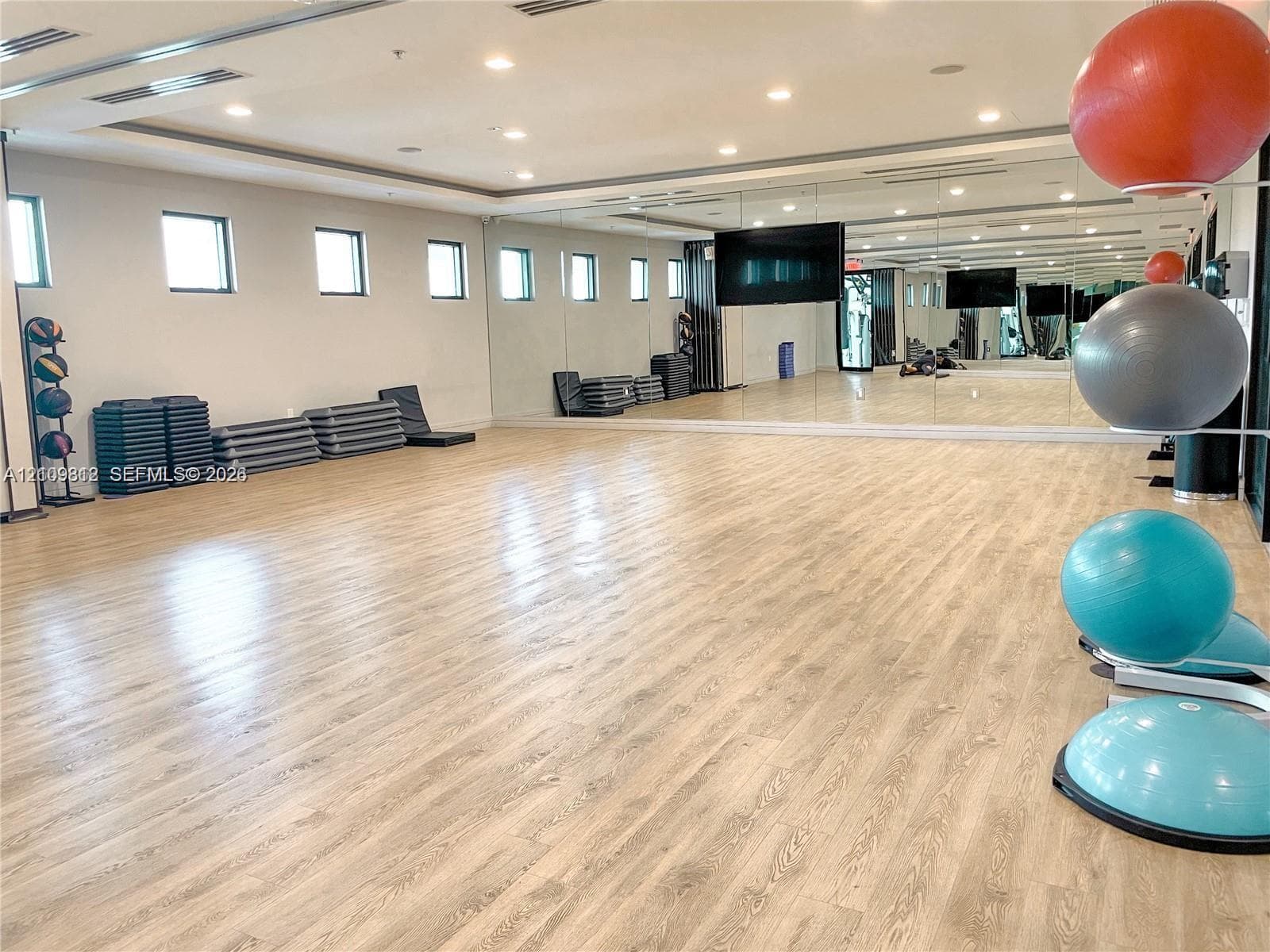 Spacious fitness studio featuring wood-finish flooring, full-wall mirrors, recessed lighting, and multiple windows