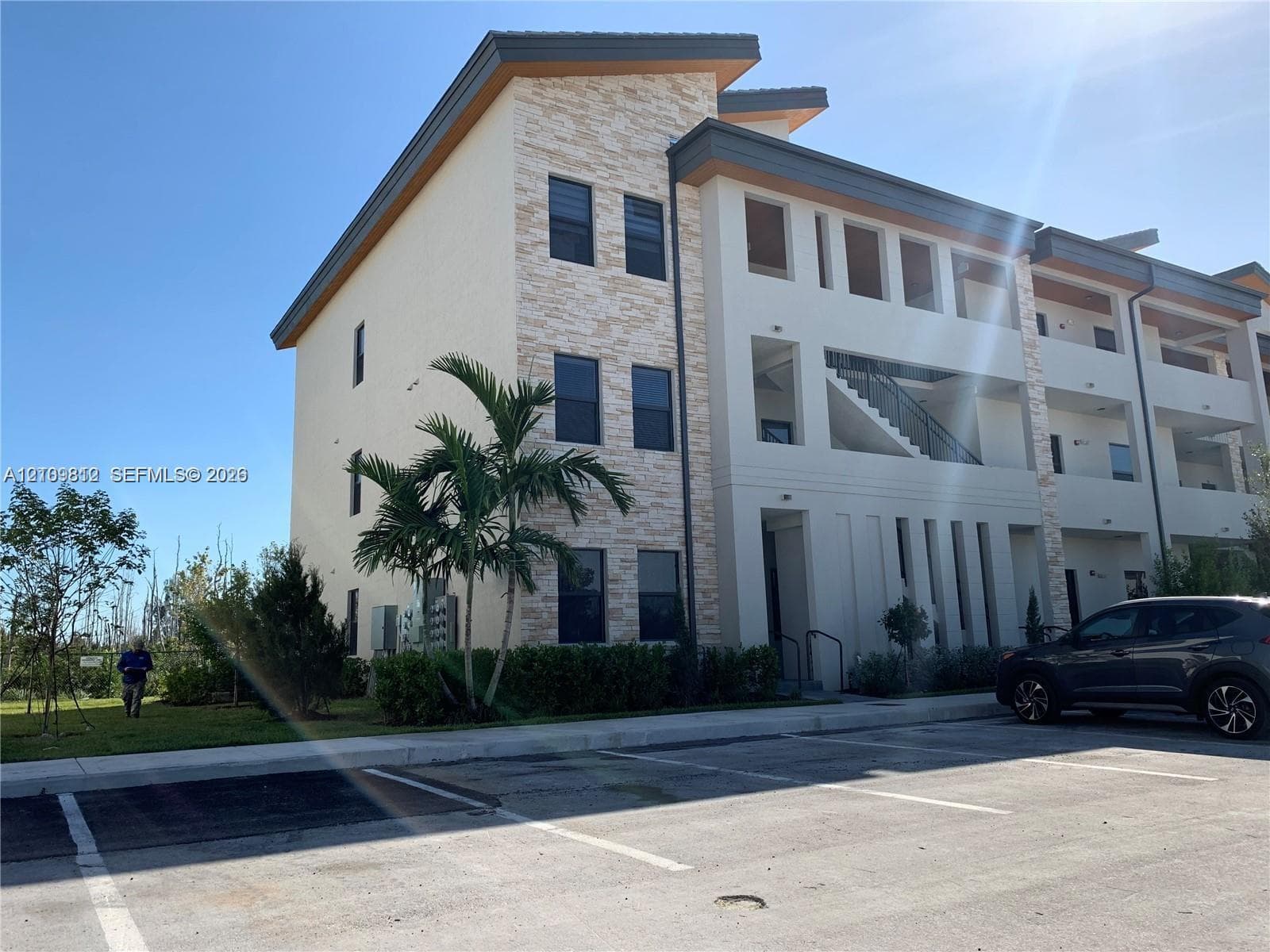 Multi-story exterior featuring a contemporary facade with stacked stone accents, smooth stucco finish, recessed balconies, and integrated stairwell detailing