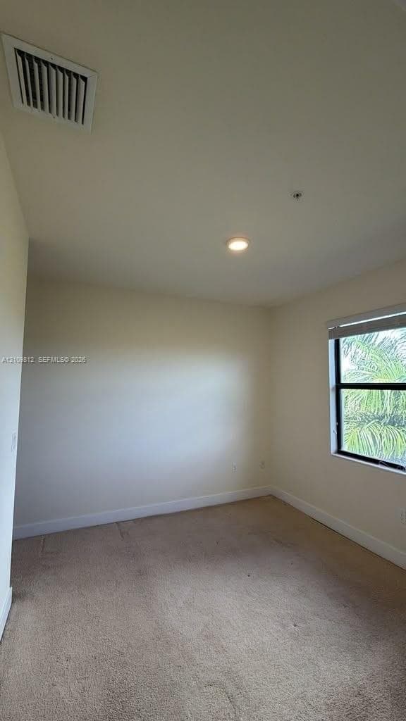Neutral-toned interior space featuring wall-to-wall carpeting, a recessed ceiling light, and a single window with dark framing