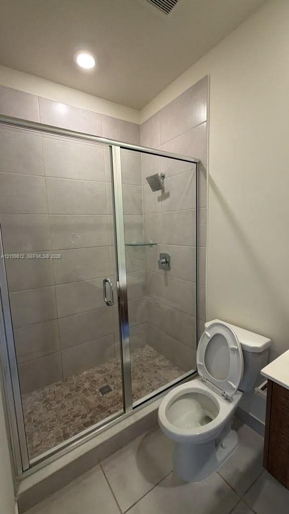 Walk-in shower with floor-to-ceiling tile surround, glass enclosure, integrated glass shelving, and pebble-textured shower floor, complemented by neutral tile flooring