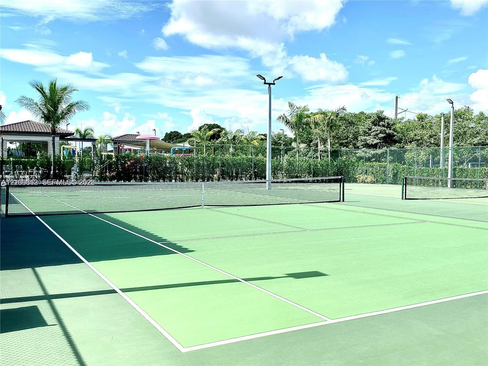 Tennis court featuring a high-contrast hard surface, perimeter fencing, and elevated pole lighting