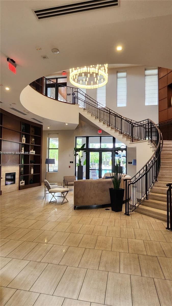 Grand foyer featuring a sweeping curved staircase with wrought-iron railing, floor-to-ceiling built-in shelving, tile flooring, and a tiered chandelier