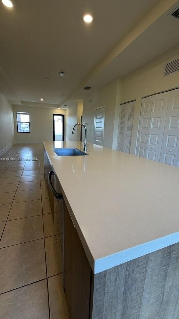 Kitchen island featuring a solid-surface countertop, under-mount stainless steel sink, arched faucet, and wood-finish cabinetry