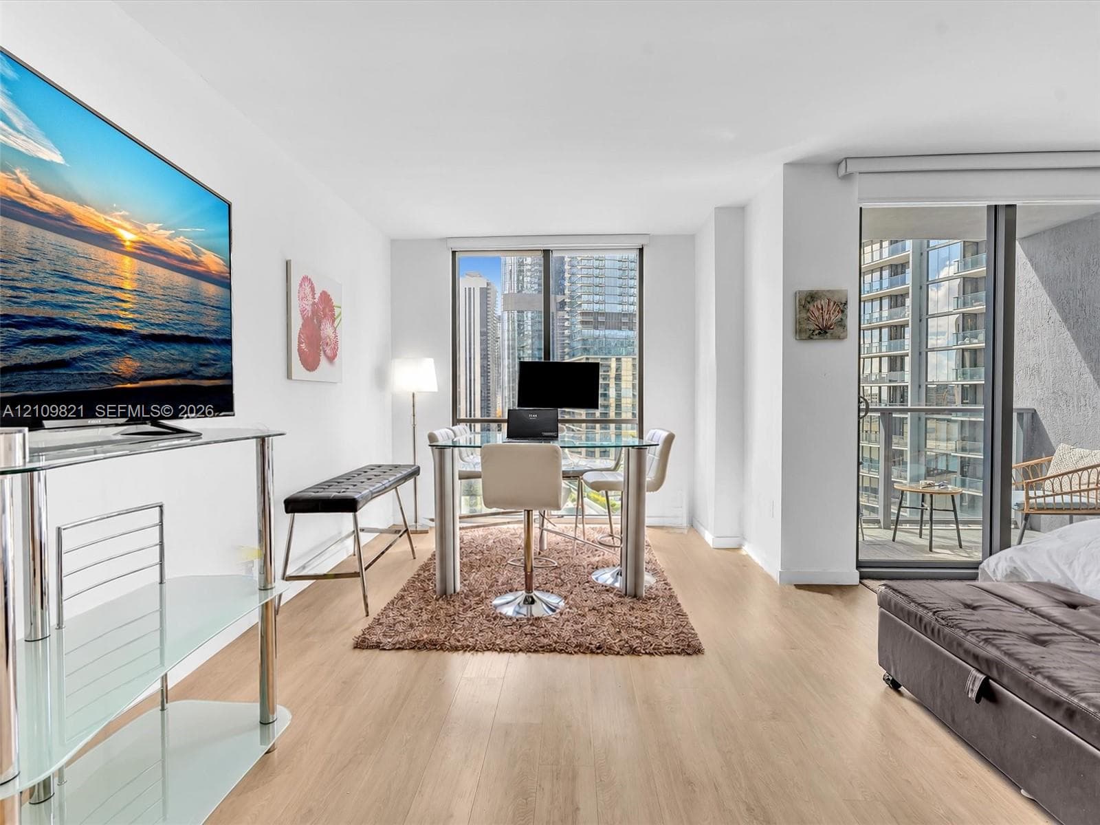 Light-filled interior featuring expansive floor-to-ceiling windows, wood-finish flooring, and a private balcony accessed via sliding glass doors