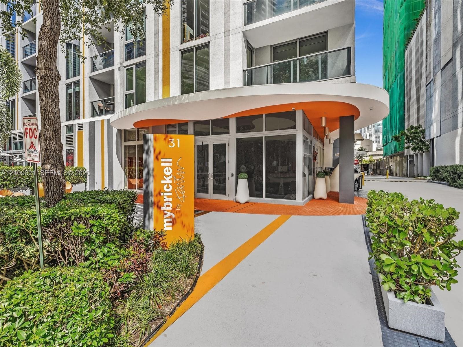 Modern architectural exterior featuring a curved canopy entrance, expansive floor-to-ceiling glass windows, concrete hardscaping, and professional exterior landscaping