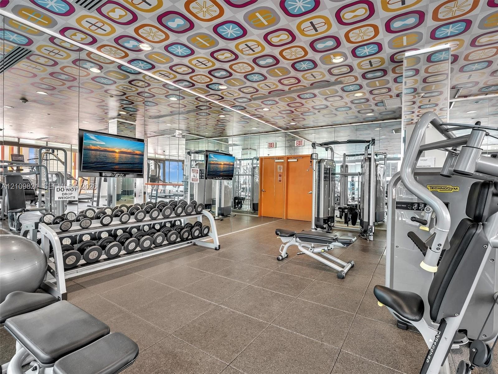 Fitness center featuring a patterned drop ceiling, neutral large-format floor tiles, recessed lighting, and mirrored wall panels