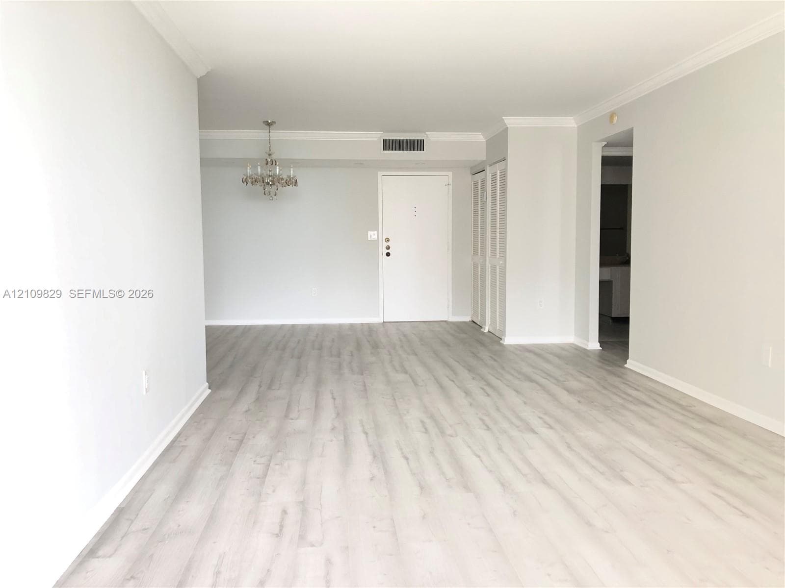 Open-concept interior featuring light wood-finish flooring, crown molding, and a suspended multi-arm light fixture