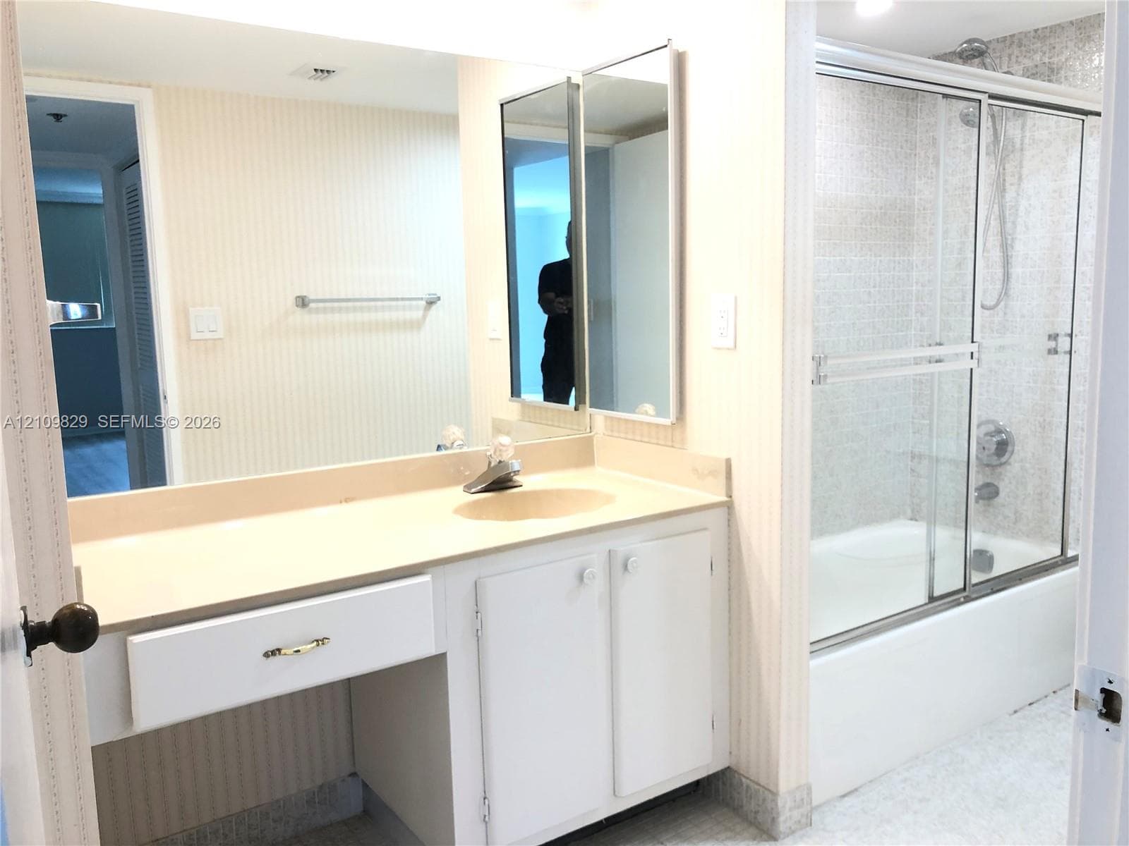 Bathroom featuring a single-sink vanity with solid-surface countertop, full-width wall mirror, medicine cabinet, and a tiled shower-tub combination with sliding glass doors