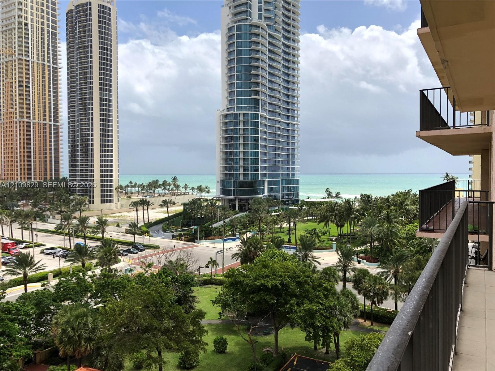 Balcony featuring a metal railing and tile flooring, oriented toward a coastal cityscape with palm trees and water frontage