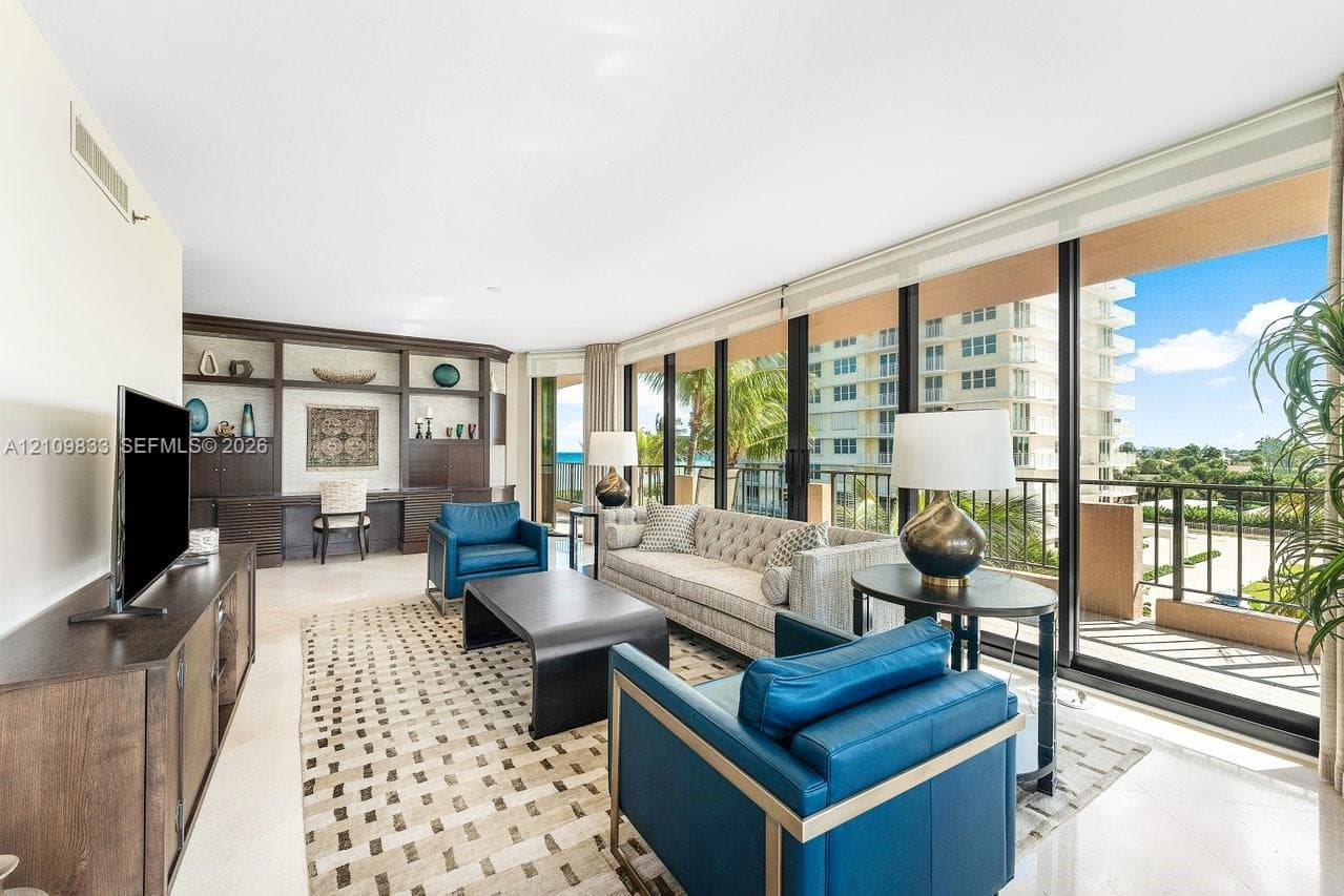 Living area featuring floor-to-ceiling windows, full-wall custom dark wood built-in cabinetry with integrated desk space, and neutral stone-finish flooring
