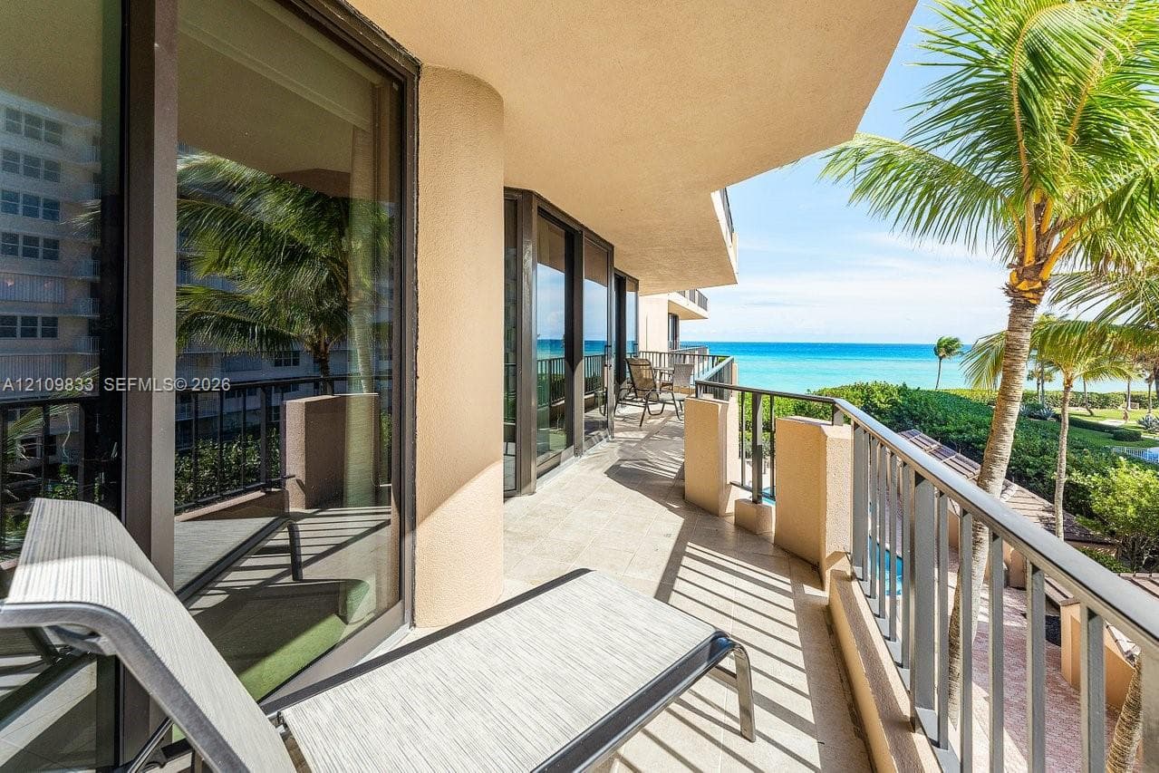 Covered balcony featuring tile flooring, full-height glass sliding doors, and metal railings, overlooking the ocean