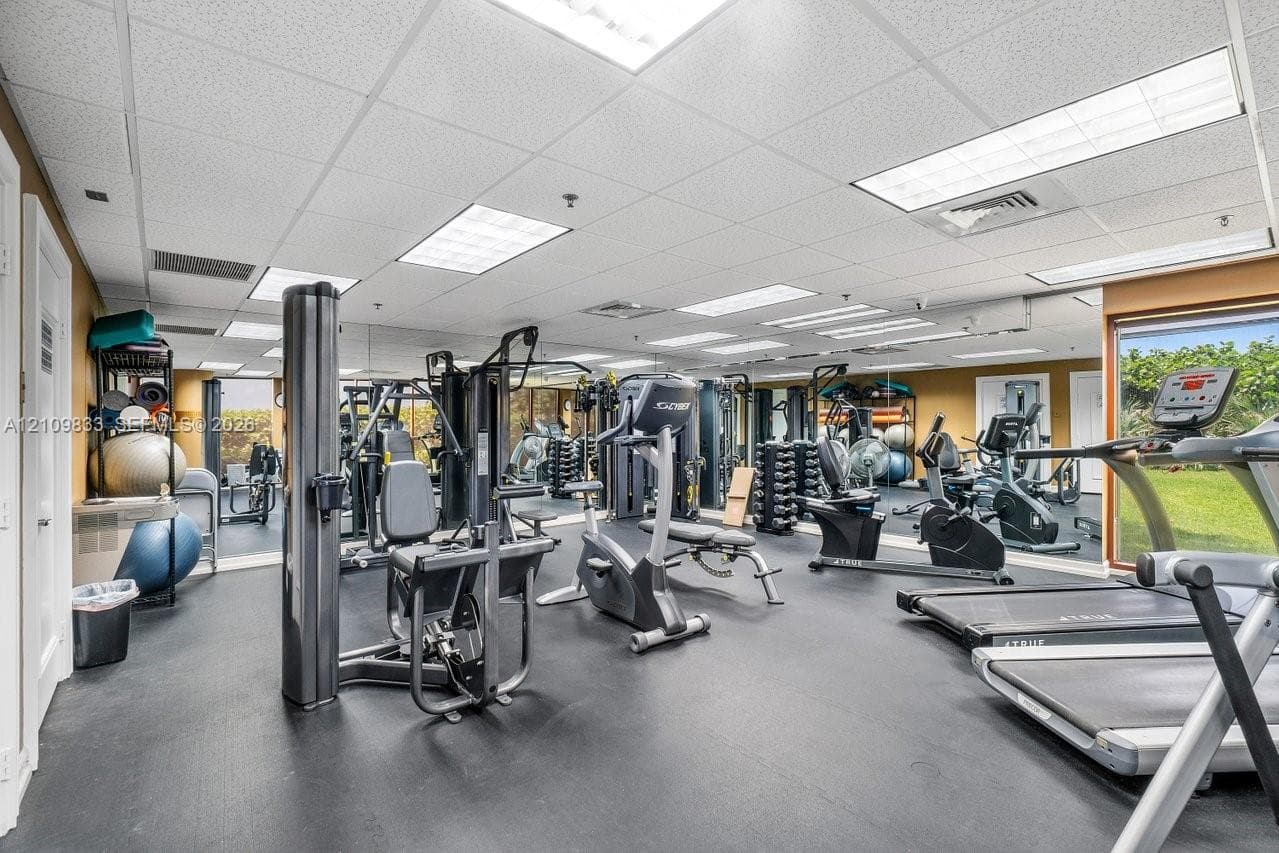 Fitness center featuring rubber flooring, mirrored walls, drop ceiling panels, and floor-to-ceiling windows