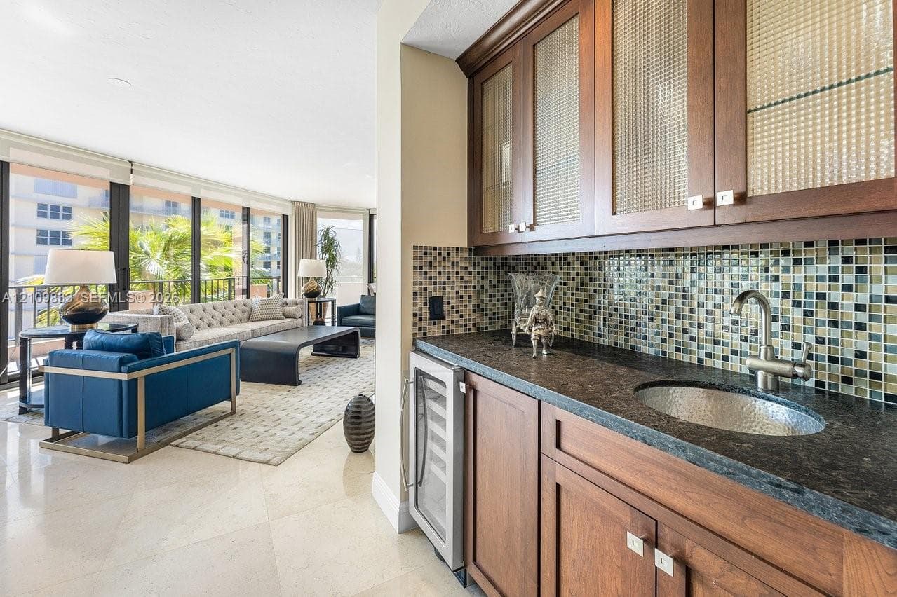 Wet bar featuring wood cabinetry, textured glass cabinet fronts, stone countertop, hammered metal sink, and mosaic tile backsplash