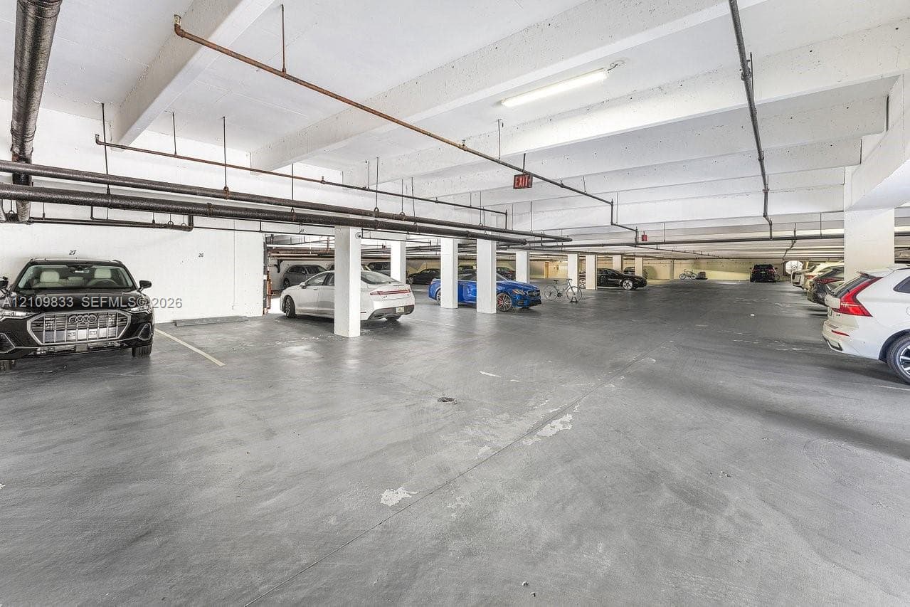 Covered parking garage featuring concrete flooring, structural support columns, and overhead linear lighting fixtures