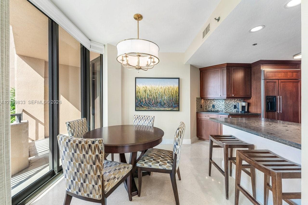 Open-concept kitchen area featuring dark wood cabinetry, stone countertops, breakfast bar, tile backsplash, and floor-to-ceiling glass panel walls