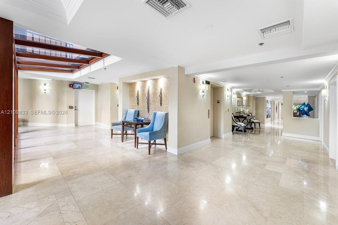 Spacious lobby featuring polished stone flooring, recessed ceiling lighting, a wood-beam architectural detail, and a decorative alcove with vertical wall accents