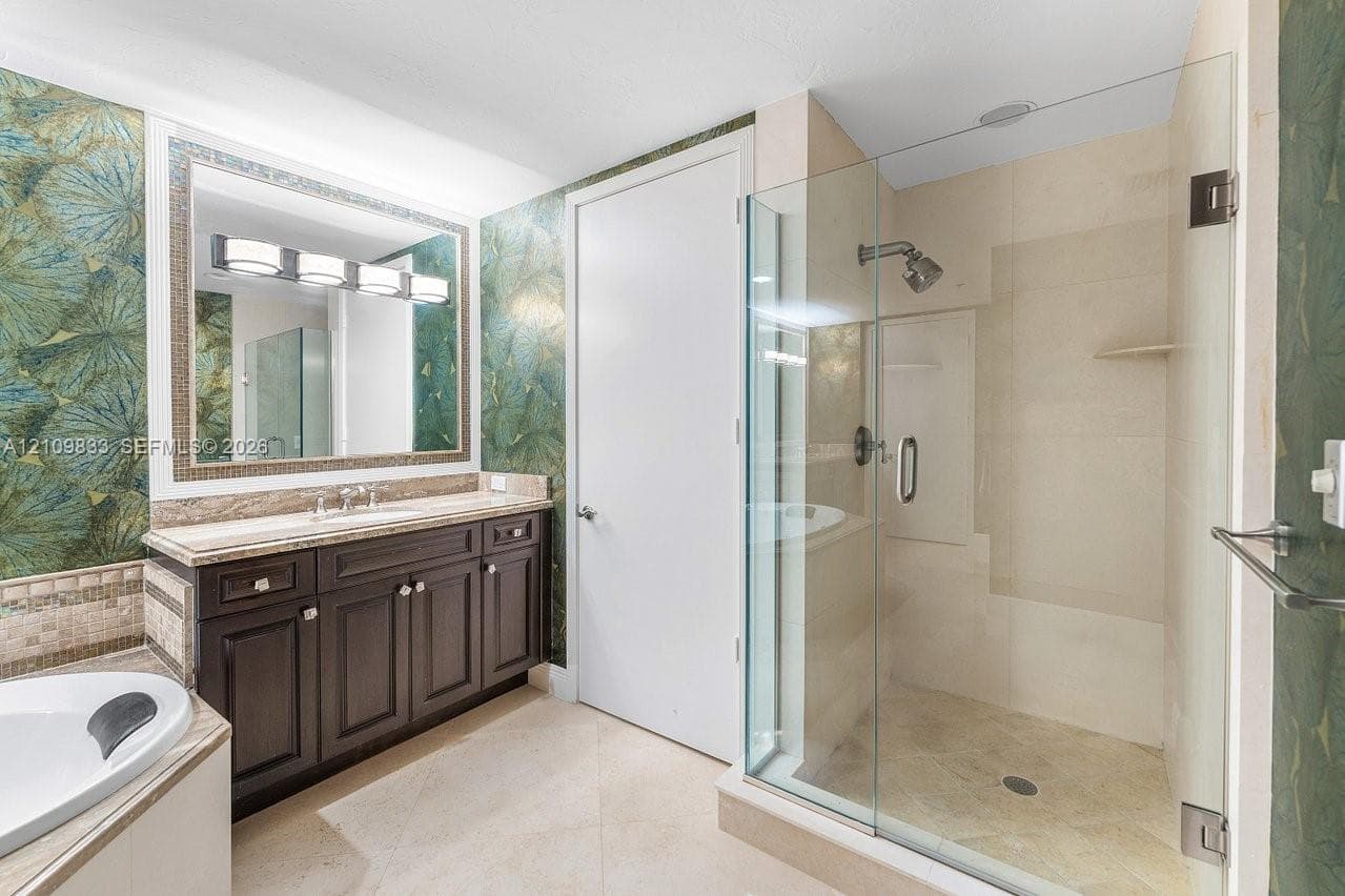 Dark wood cabinetry with stone-finish vanity top, glass-enclosed shower with tile surround, large-format tile flooring, and integrated soaking tub